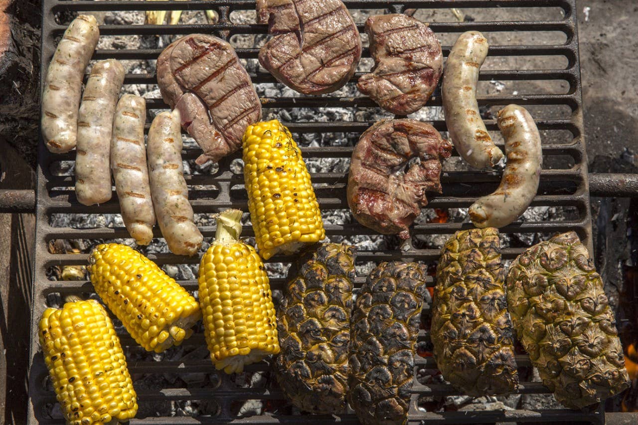 Overhead view of meats, pineapple and corn on grill above campfire
