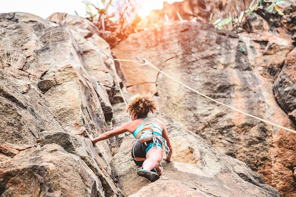 Young woman climbing a rock wall in a canyon - Strong climber training outdoor - Travel, female power and extreme dangerous sport concept - Focus on her head