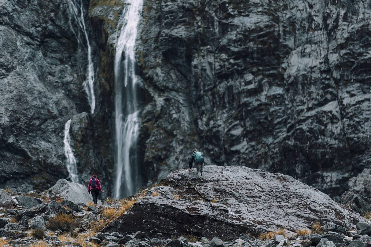 An athletic couple climbs to the basin of a waterfall