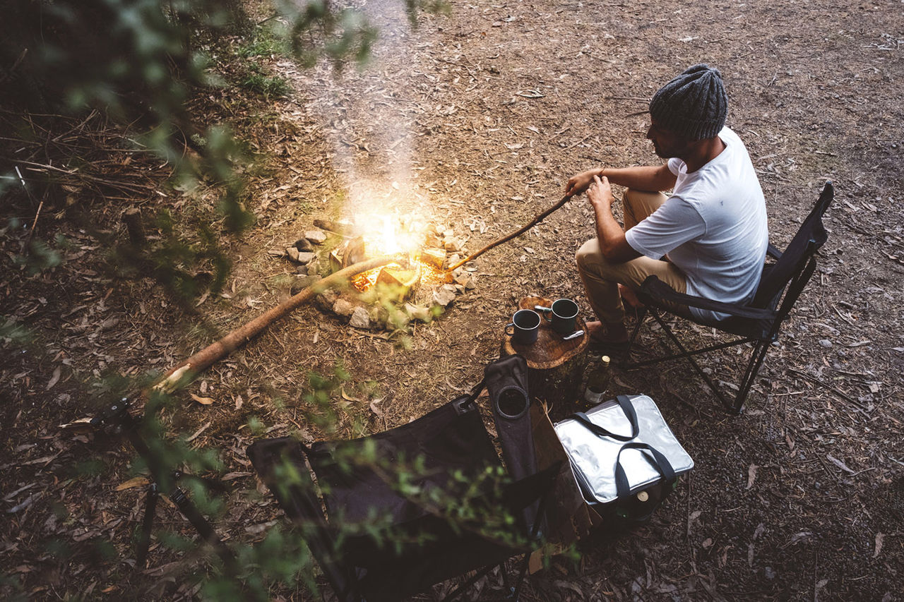 High angle view of hiker sitting on camping chair by campfire in forest